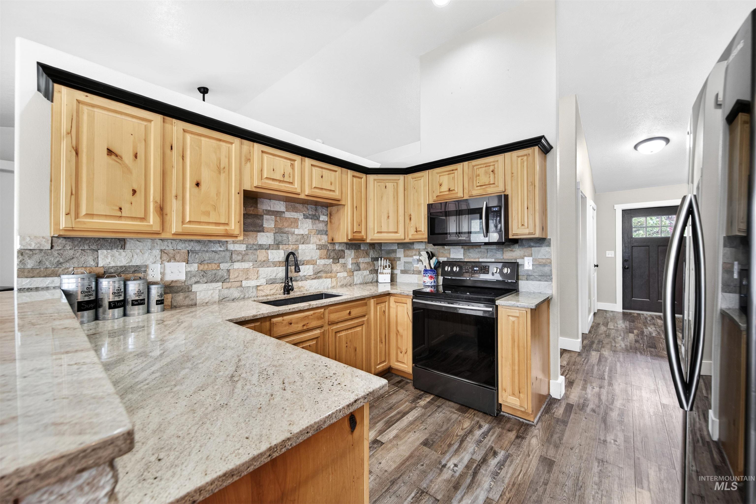 4 Round Up Circle Boise, ID 83716 - Photo 10 of 47 Kitchen featuring natural wood cabinetry with black trim, stone-finish backsplash, light-toned countertops, and wood-finish flooring