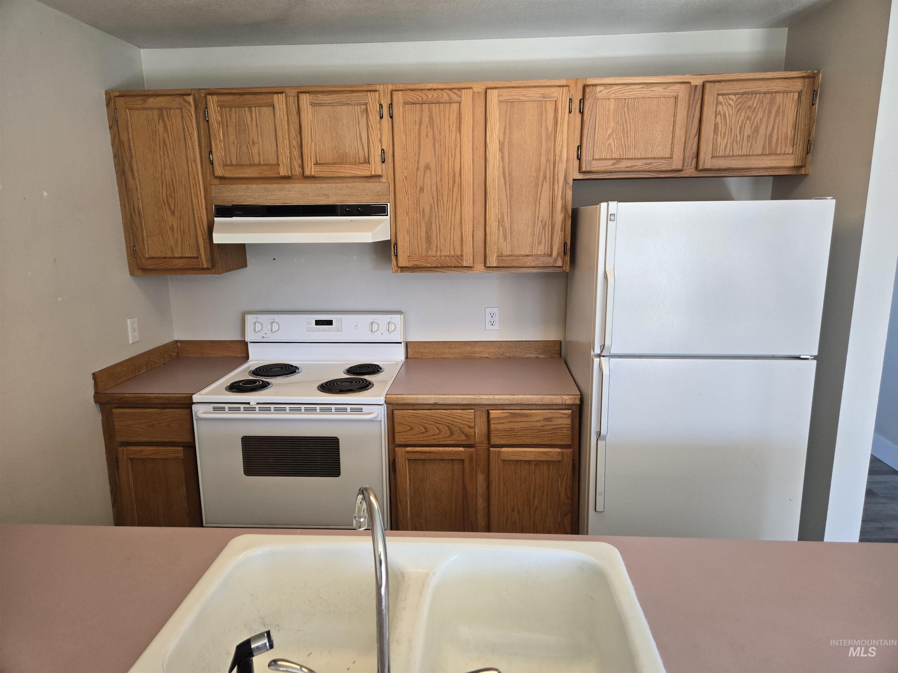 259 Pheasant Road West, Unit 50 Twin Falls, ID 83301 - Photo 13 of 23 Kitchen with white appliances, under cabinet range hood, brown cabinets, and light countertops