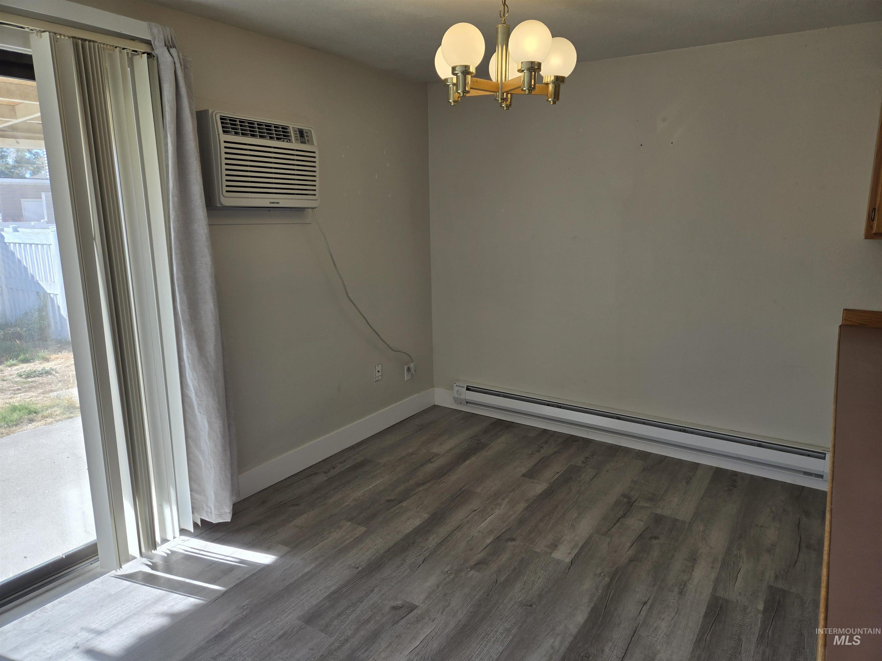 259 Pheasant Road West, Unit 50 Twin Falls, ID 83301 - Photo 14 of 23 Unfurnished dining area with a baseboard radiator, dark wood finished floors, a chandelier, and a wall mounted AC