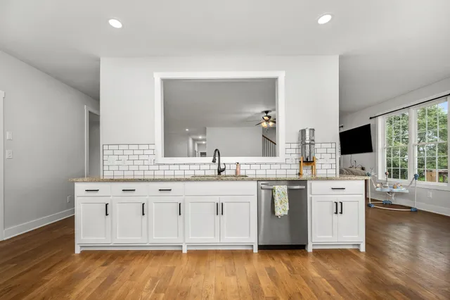 a kitchen with stainless steel appliances granite countertop a stove top oven a sink a refrigerator white cabinets and wooden floor