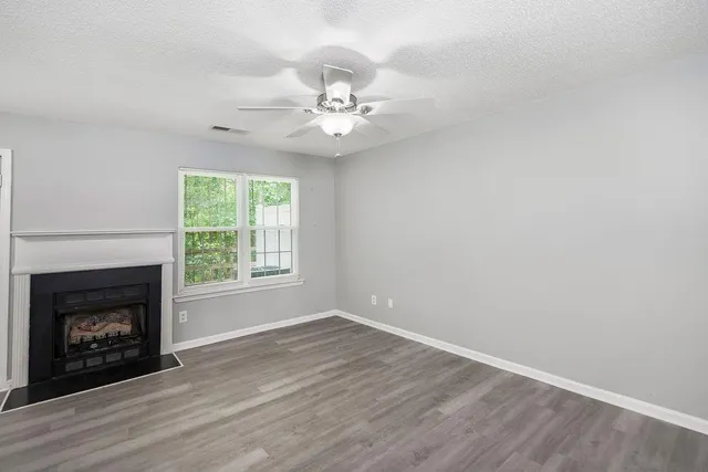 an empty room with wooden floor fireplace cabinet and windows