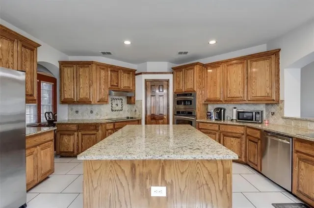 a kitchen with stainless steel appliances granite countertop a stove top oven a sink dishwasher and a refrigerator with wooden cabinets