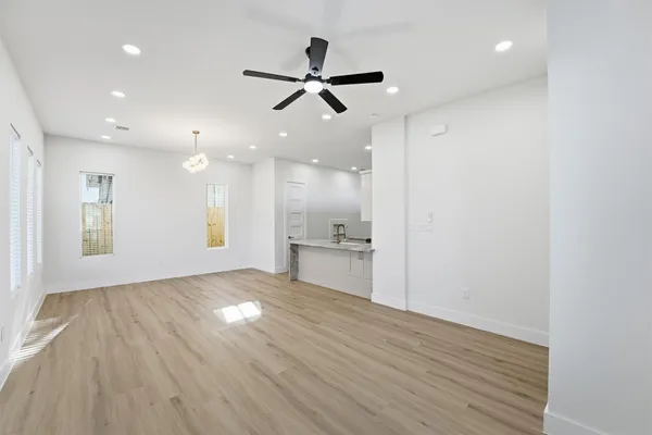 a view of an empty room and kitchen with wooden floor and a ceiling fan