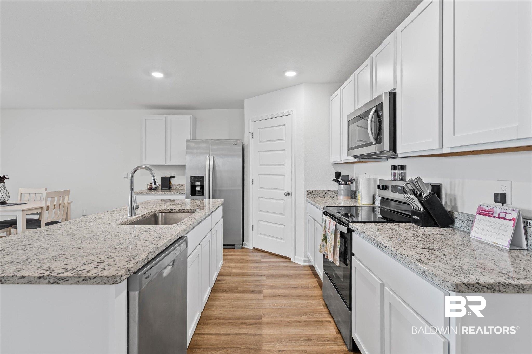 1105 Hayward Loop Foley, AL 36535 - Photo 6 of 30 Kitchen featuring appliances with stainless steel finishes, light wood-type flooring, white cabinets, an island with sink, and light stone countertops