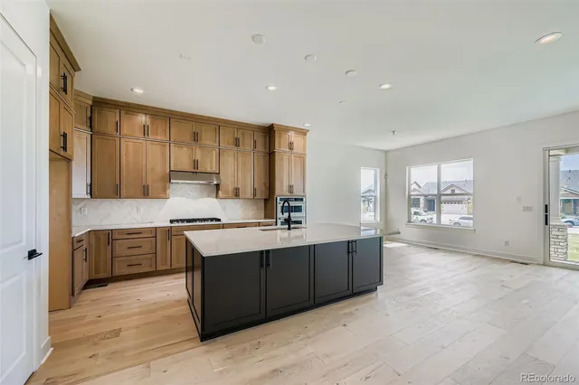 a large kitchen with stainless steel appliances granite countertop a stove top oven a sink dishwasher and a refrigerator with wooden floor