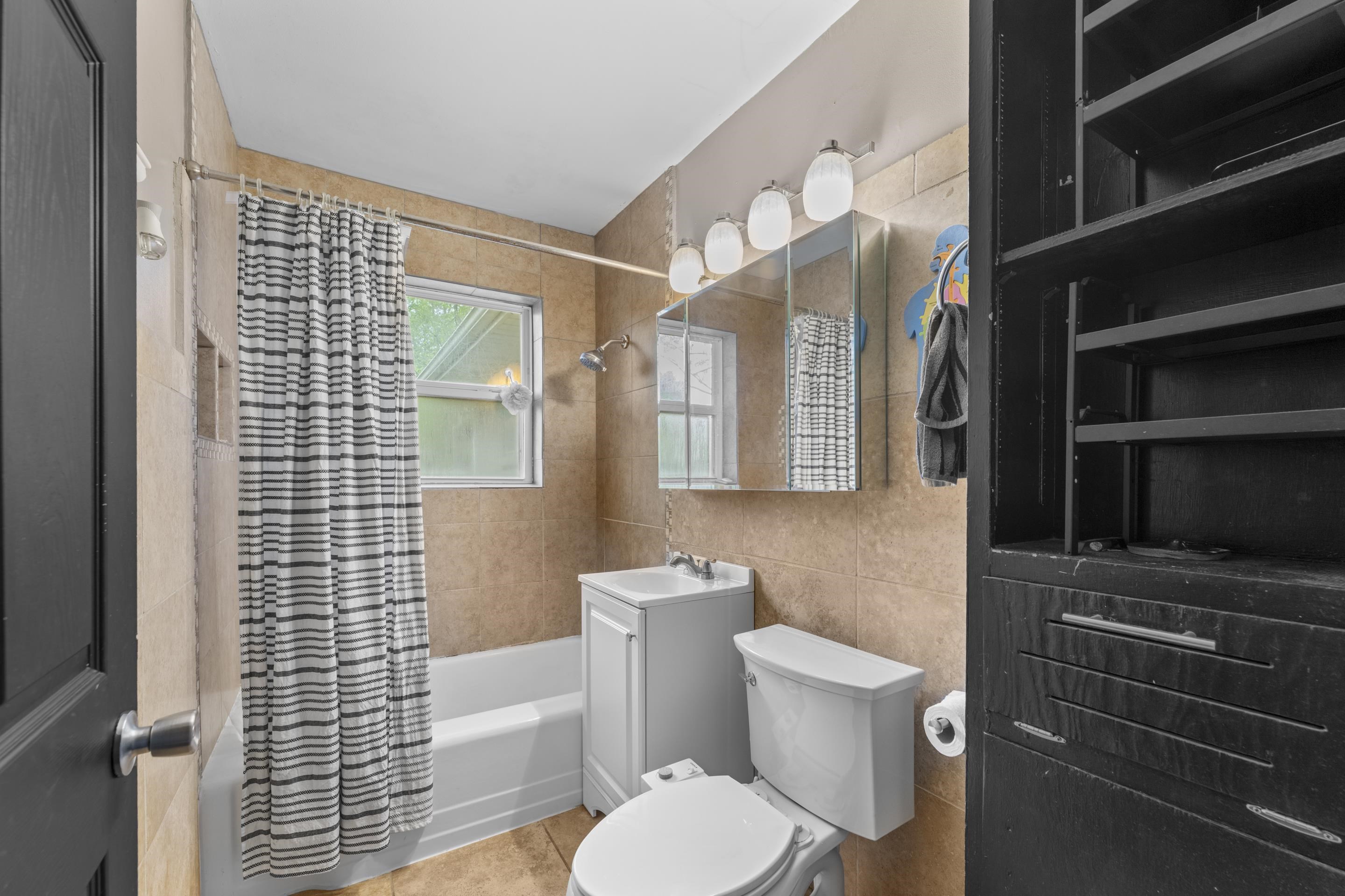1343 Dearing Road Memphis, TN 38117 - Photo 11 of 19 Bathroom featuring a tiled shower surround, a window with frosted glass, a white vanity with integrated sink, a toilet, and built-in shelving with drawers