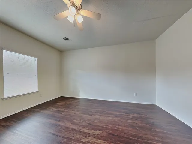 a view of an empty room with wooden floor and a ceiling fan
