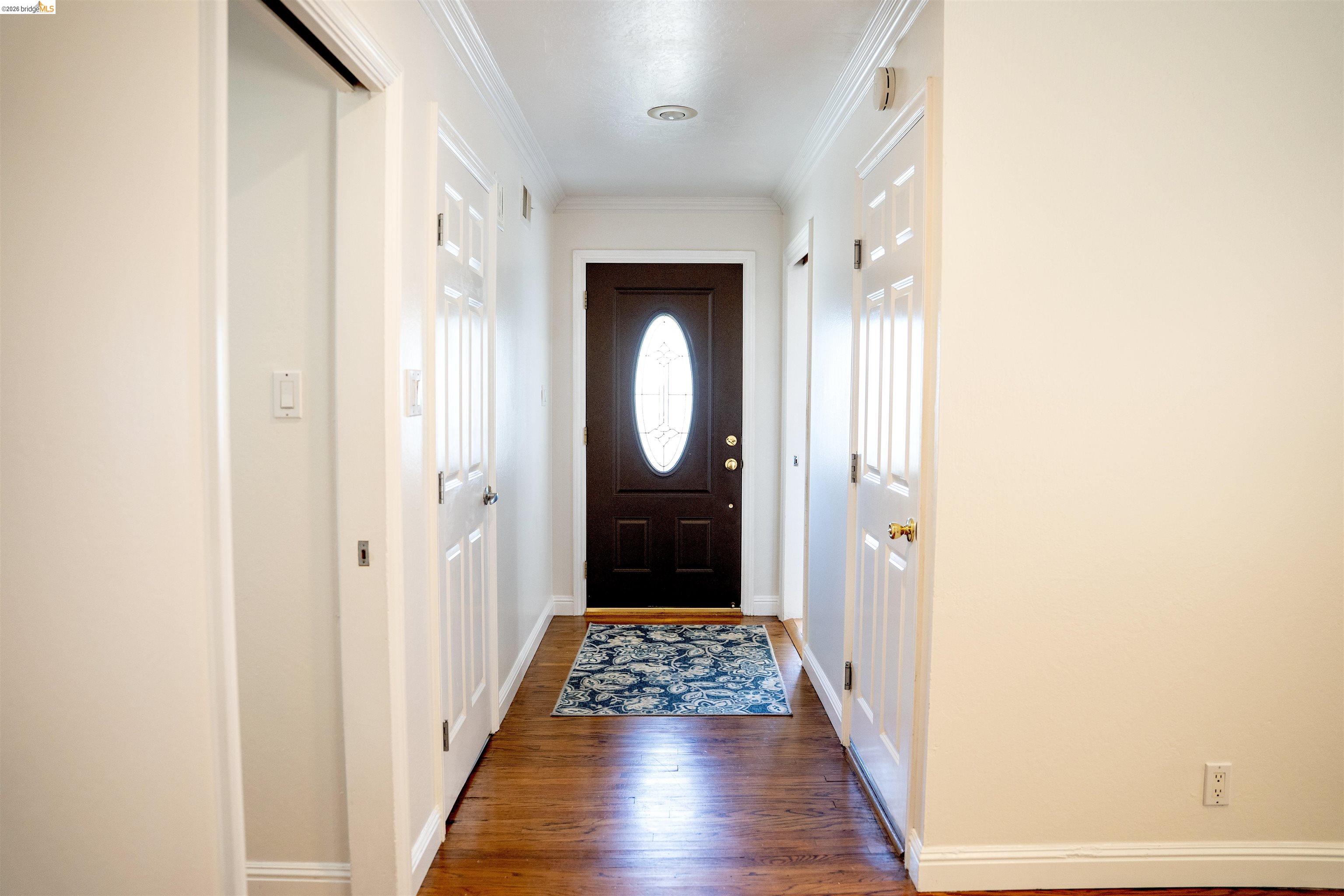 64 Washington Street Novato, CA 94947 - Photo 9 of 21 Entryway featuring a dark wood front door with an oval glass insert, wood-finish flooring, white crown molding, and white interior doors with brass hardware