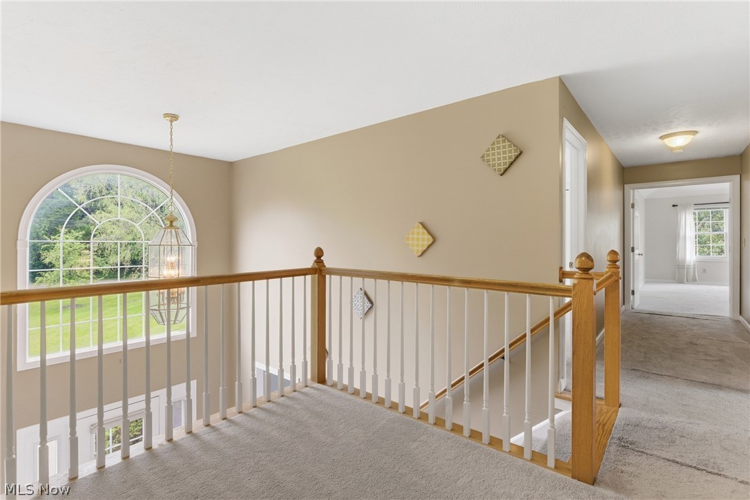 11678 Dunham Road Northfield, OH 44067 - Photo 18 of 38 Upper-level landing featuring a grand arched window, wood-finish handrails, white balusters, and soft carpet flooring
