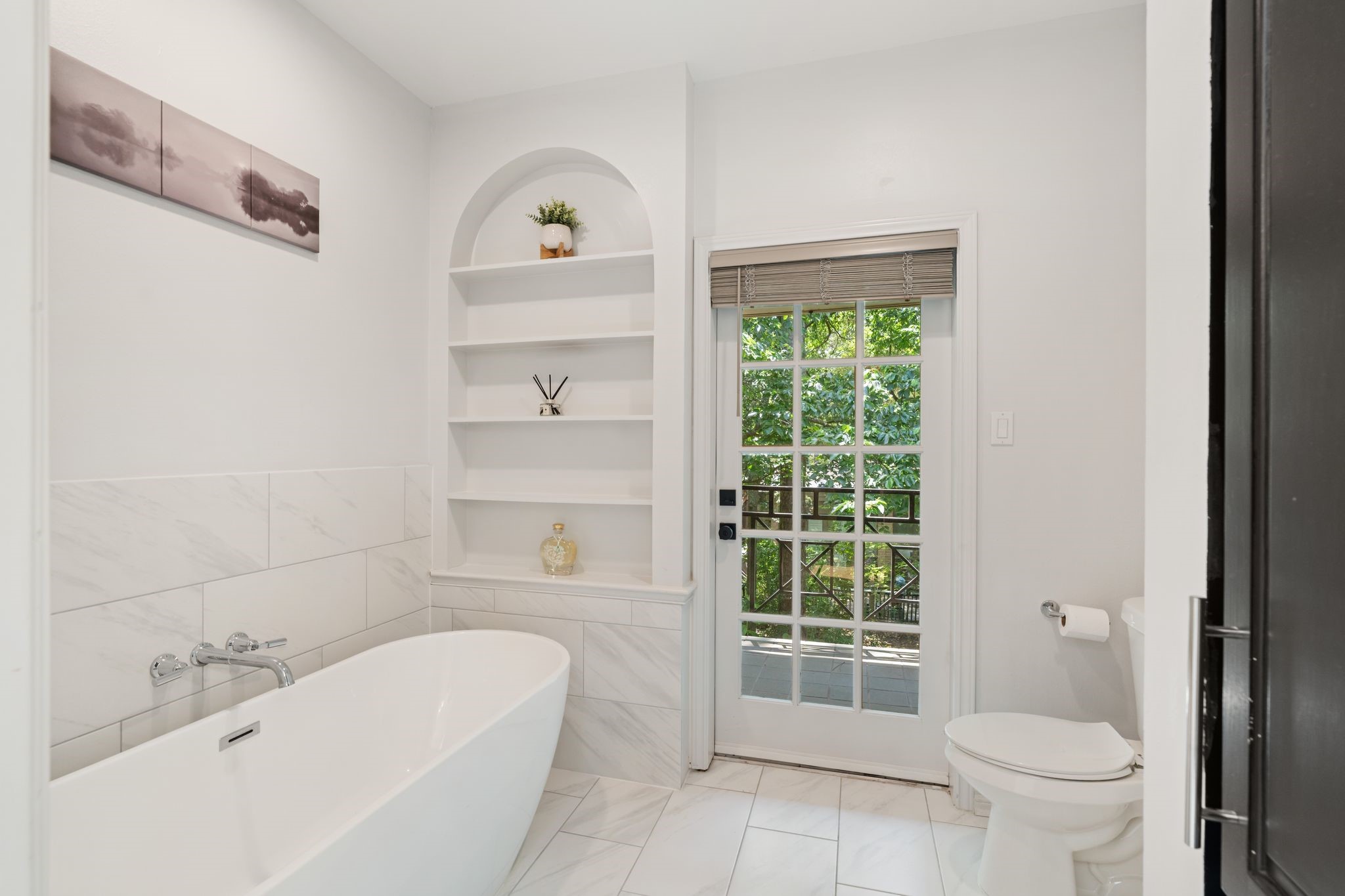 201 Vanderpool Lane, Unit 137 Houston, TX 77024 - Photo 24 of 42 A freestanding soaking tub framed by marble-look wall tile creates a true spa moment in the primary bath. Thoughtful display cabinetry adds warmth and storage, while private balcony access directly off the tub area brings the outdoors in for the ultimate retreat-style experience.