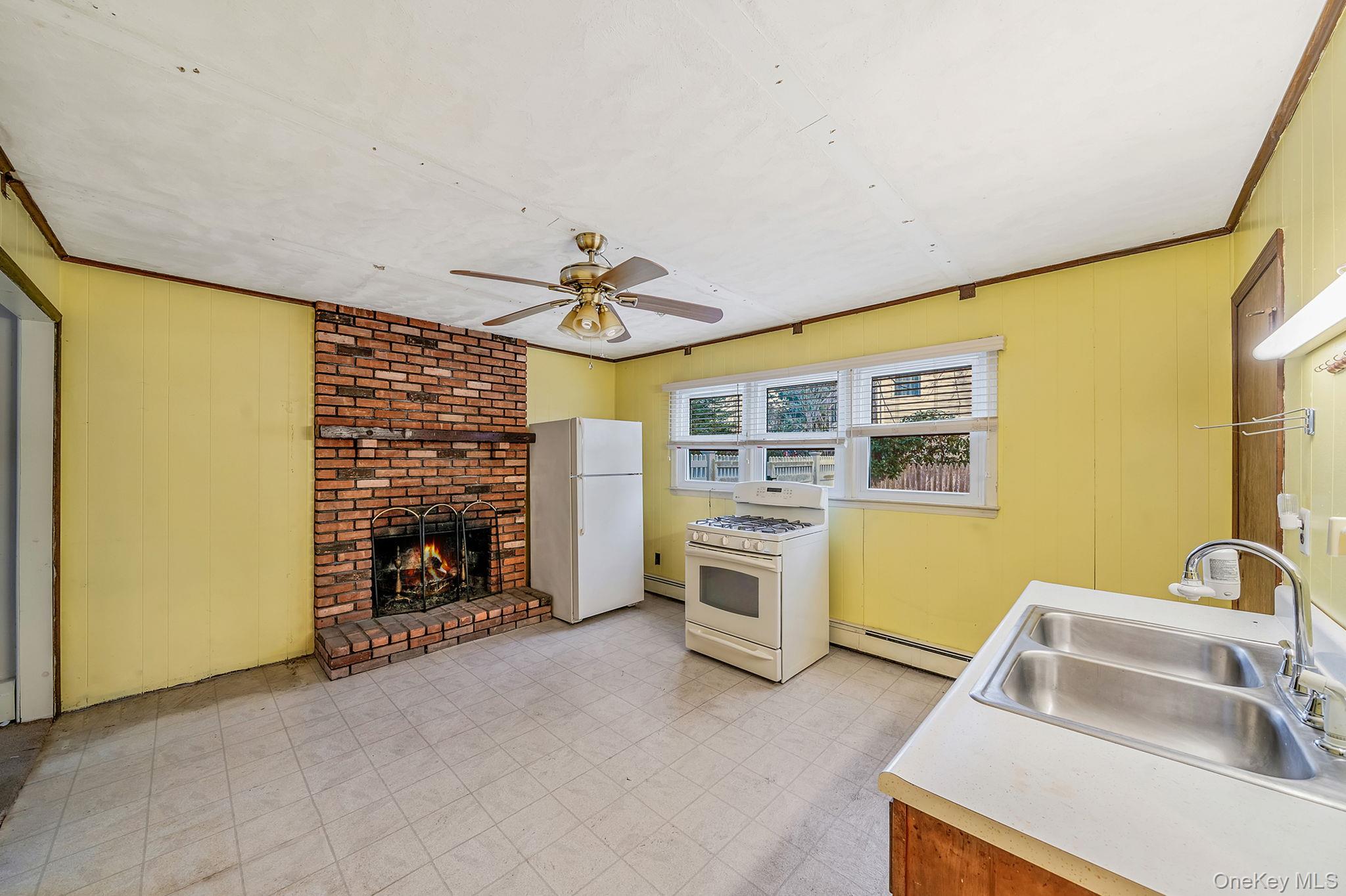 120 Rustic Road Port Jefferson, NY 11777 - Photo 22 of 45 Kitchen featuring wood walls, white appliances, a ceiling fan, a fireplace, and ornamental molding