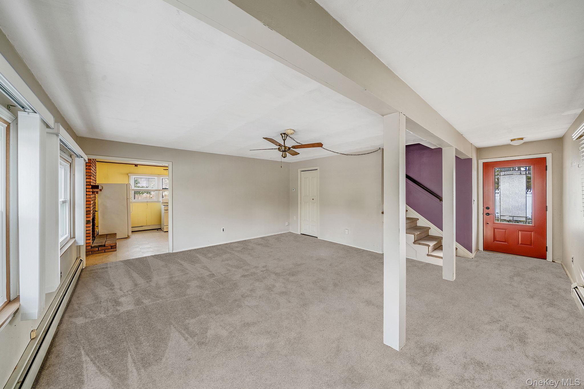 120 Rustic Road Port Jefferson, NY 11777 - Photo 25 of 45 Unfurnished living room featuring a baseboard heating unit, stairs, healthy amount of natural light, and light carpet