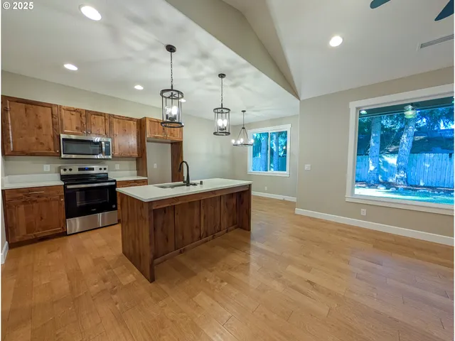 a open kitchen with stainless steel appliances kitchen island granite countertop a stove top oven a sink dishwasher a dining table and chairs with wooden floor