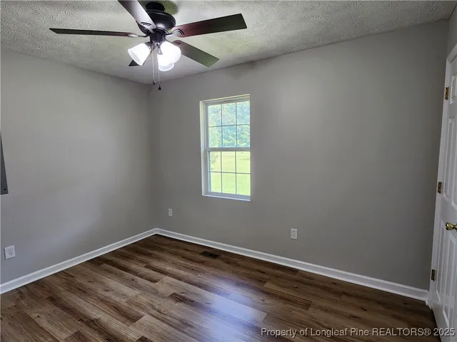 an empty room with wooden floor fan and windows