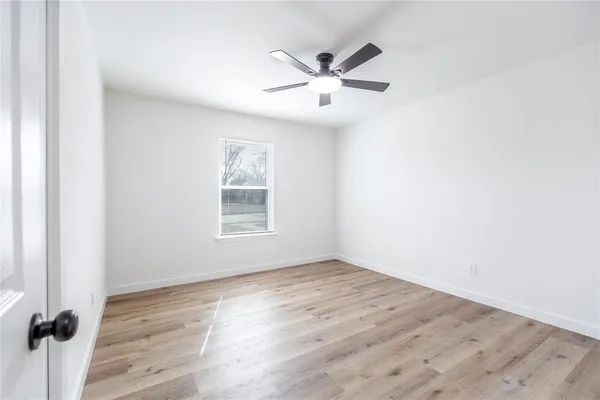 an empty room with wooden floor fan and windows
