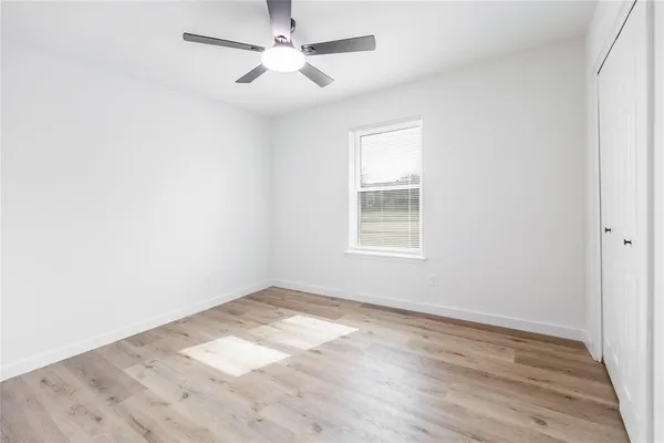 an empty room with wooden floor ceiling fan and windows