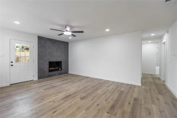 an empty room with wooden floor a ceiling fan a fireplace and windows