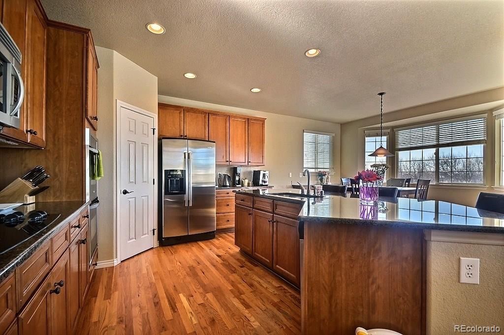 17874 West 77th Lane Arvada, CO 80007 - Photo 12 of 33 a kitchen with stainless steel appliances granite countertop a refrigerator a sink dishwasher a stove and a dining table with wooden floor