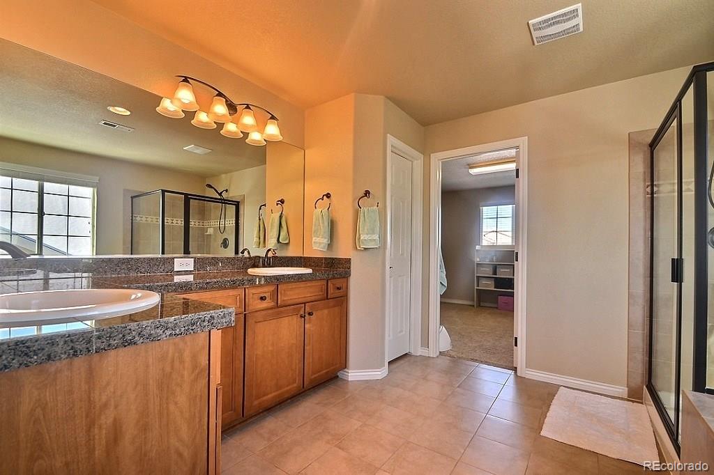 17874 West 77th Lane Arvada, CO 80007 - Photo 22 of 33 a spacious bathroom with a granite countertop sink a mirror and a shower