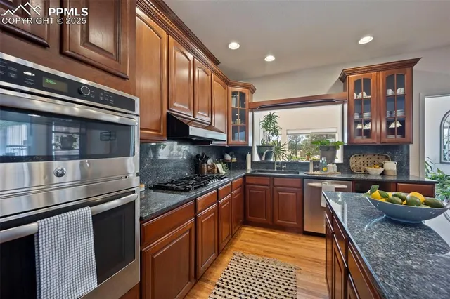 a kitchen with a refrigerator a stove top oven a sink dishwasher with couches and dining table with wooden floor