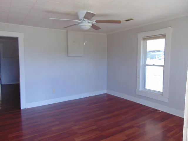 an empty room with wooden floor fan and windows