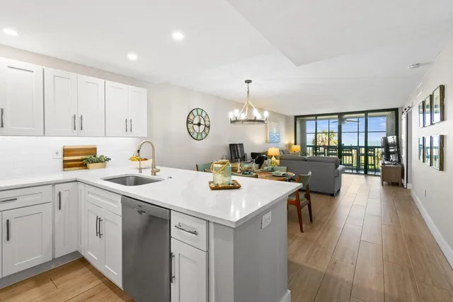 a view of a kitchen counter space a sink dishwasher a stove and a dining table with wooden floor