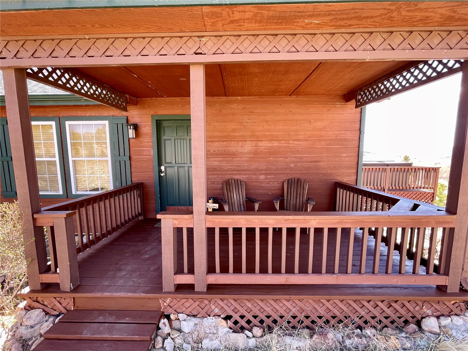 1301 Sheep Ridge Road Fairplay, CO 80440 - Photo 39 of 49 Front porch featuring natural wood siding and decking, a dark green entry door, decorative latticework, and white-framed windows with dark green shutters