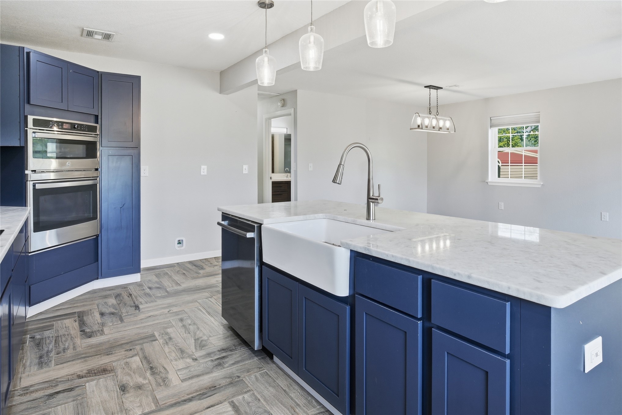 81232 South 4775 Road Stilwell, OK 74960 - Photo 25 of 50 Kitchen featuring blue shaker-style cabinetry, a built-in stainless steel double oven, a center island with a farmhouse sink, light-toned countertops, and wood-finish flooring in a herringbone pattern
