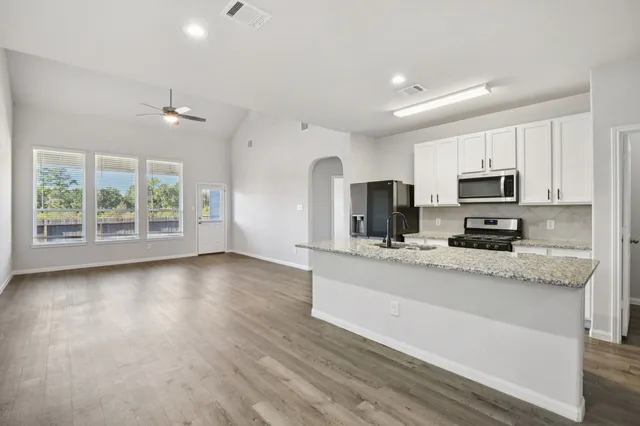 a large kitchen with stainless steel appliances granite countertop a stove a sink dishwasher a microwave oven with cabinets and wooden floor