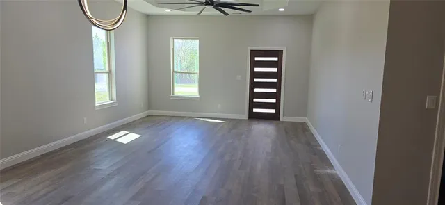 an empty room with wooden floor fan and windows