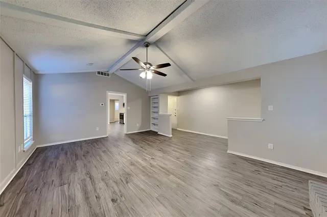 an empty room with wooden floor ceiling fan and windows