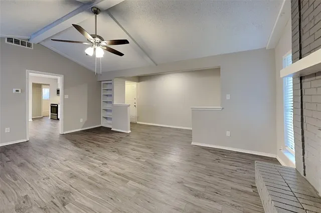 a view of an empty room with wooden floor and a ceiling fan