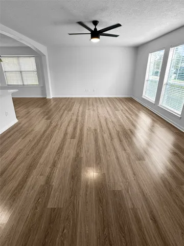 an empty room with wooden floor fan and windows