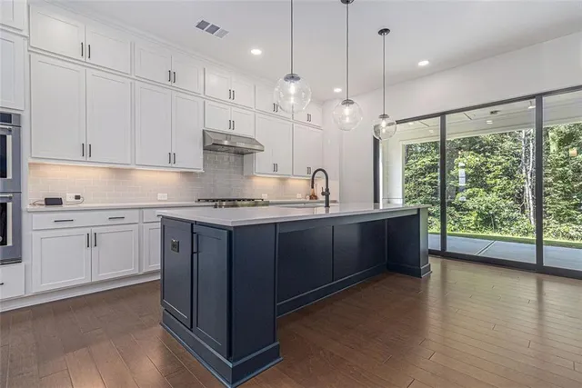 a kitchen with stainless steel appliances granite countertop a stove a sink and white cabinets with wooden floor