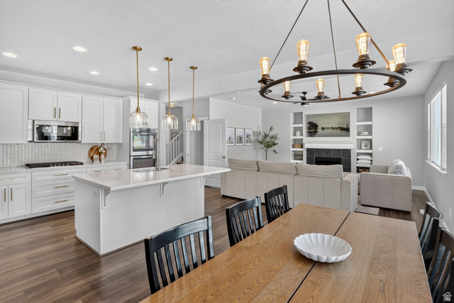 2178 Autumn Drive Mapleton, UT 84664 - Photo 11 of 48 Open-concept living space featuring wood-finish flooring, white cabinetry, stainless steel appliances, a built-in fireplace with shelving, and an overhead chandelier