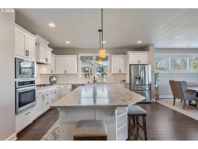 a kitchen with kitchen island a stove a refrigerator a dining table and chairs with wooden floors