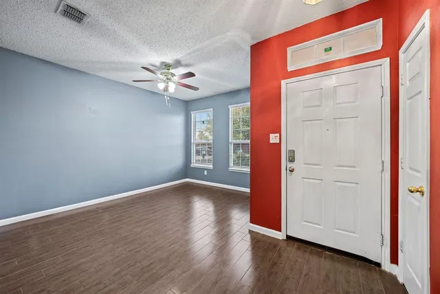 an empty room with wooden floor chandelier fan and windows