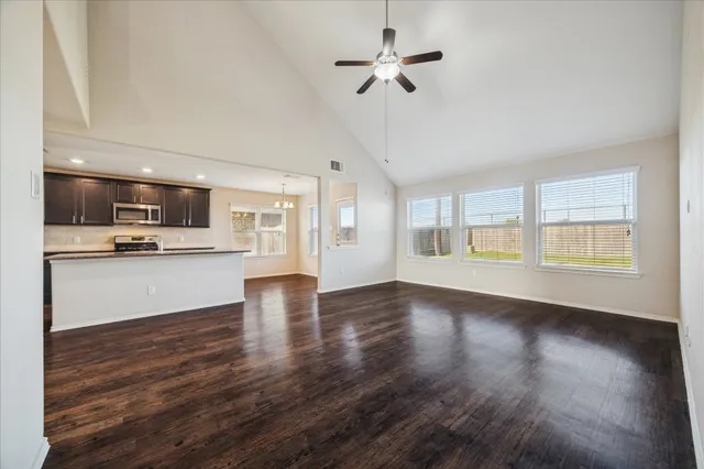 a view of an empty room with kitchen and window
