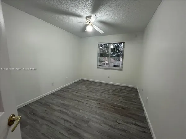 an empty room with wooden floor fan and window