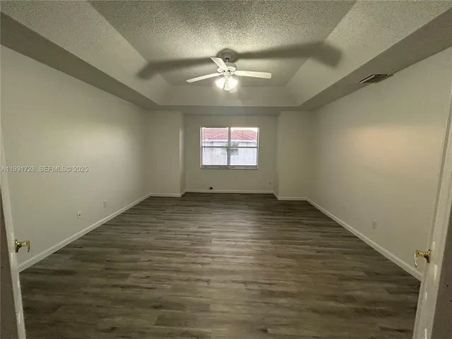 an empty room with wooden floor fan and windows