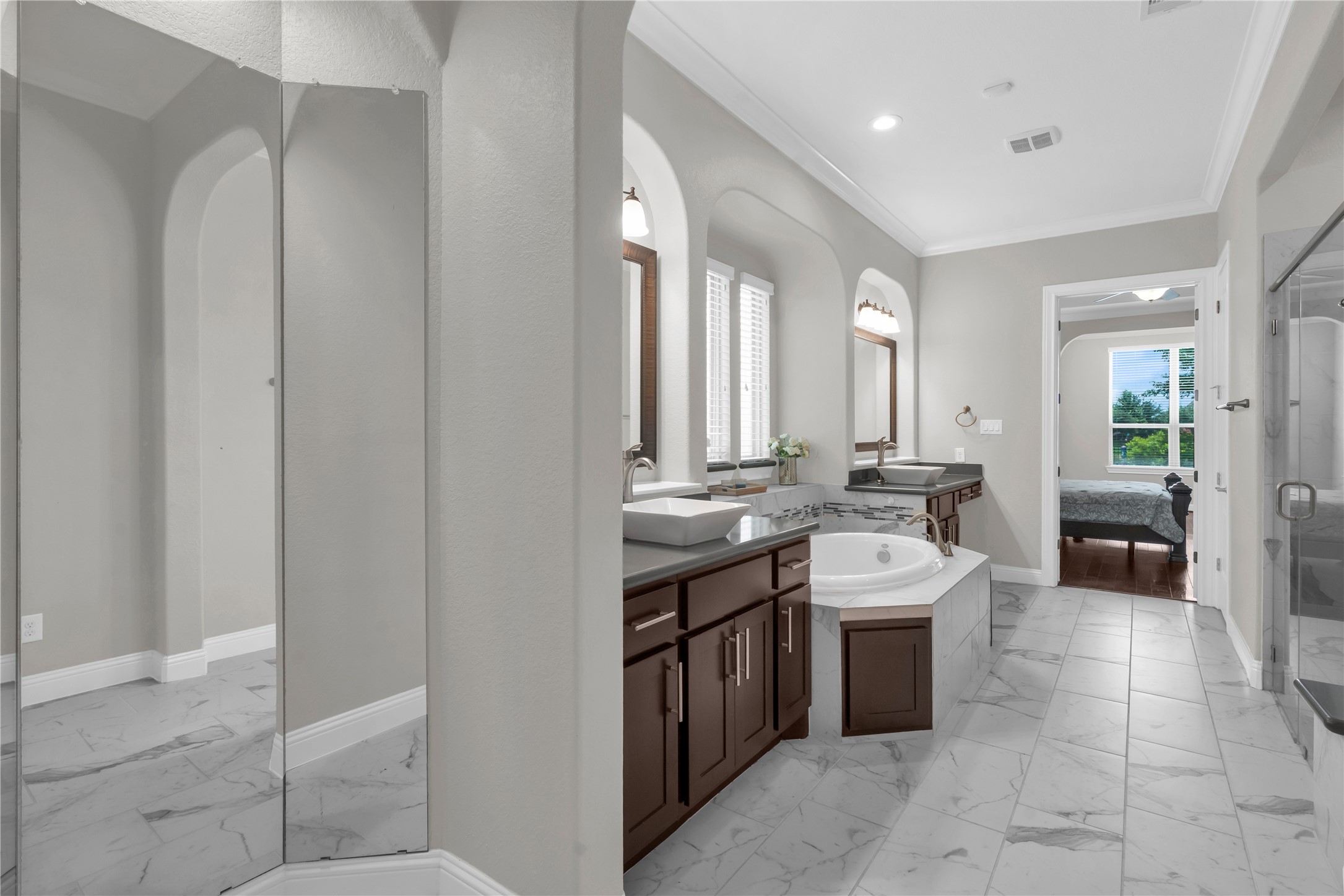 9842 Kirkstone Terrace Drive Spring, TX 77379 - Photo 17 of 34 This elegant bathroom features a spacious layout with a large soaking tub, dual vanities with modern sinks, and a glass-enclosed shower. The neutral color palette and marble floor add a touch of luxury, while arched windows provide ample natural light. The bathroom connects to a bedroom, enhancing convenience and privacy.