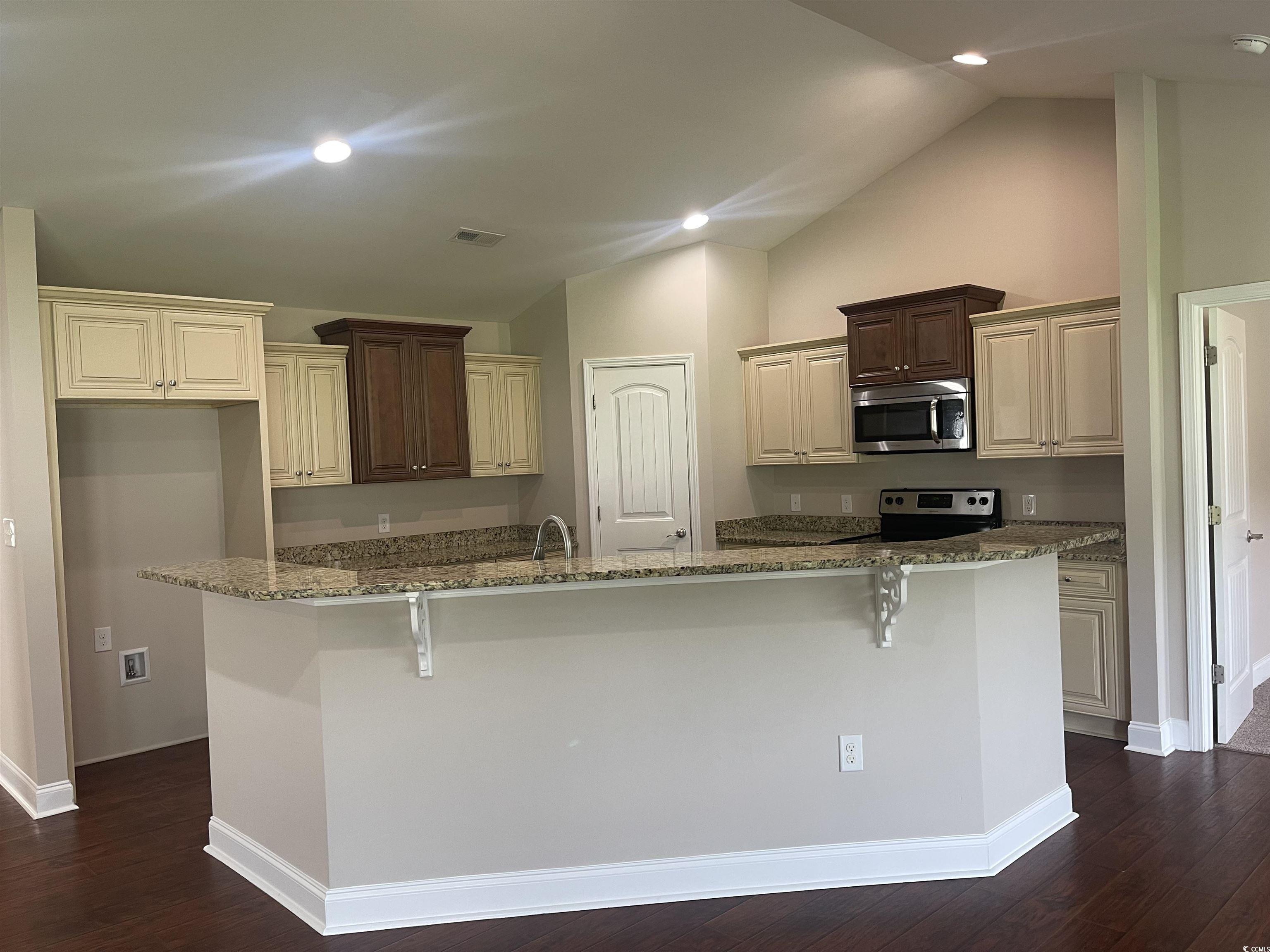128 Cloey Road Myrtle Beach, SC 29579 - Photo 14 of 22 Kitchen featuring cream cabinetry, dark stone countertops, dark wood-style floors, a kitchen breakfast bar, and vaulted ceiling