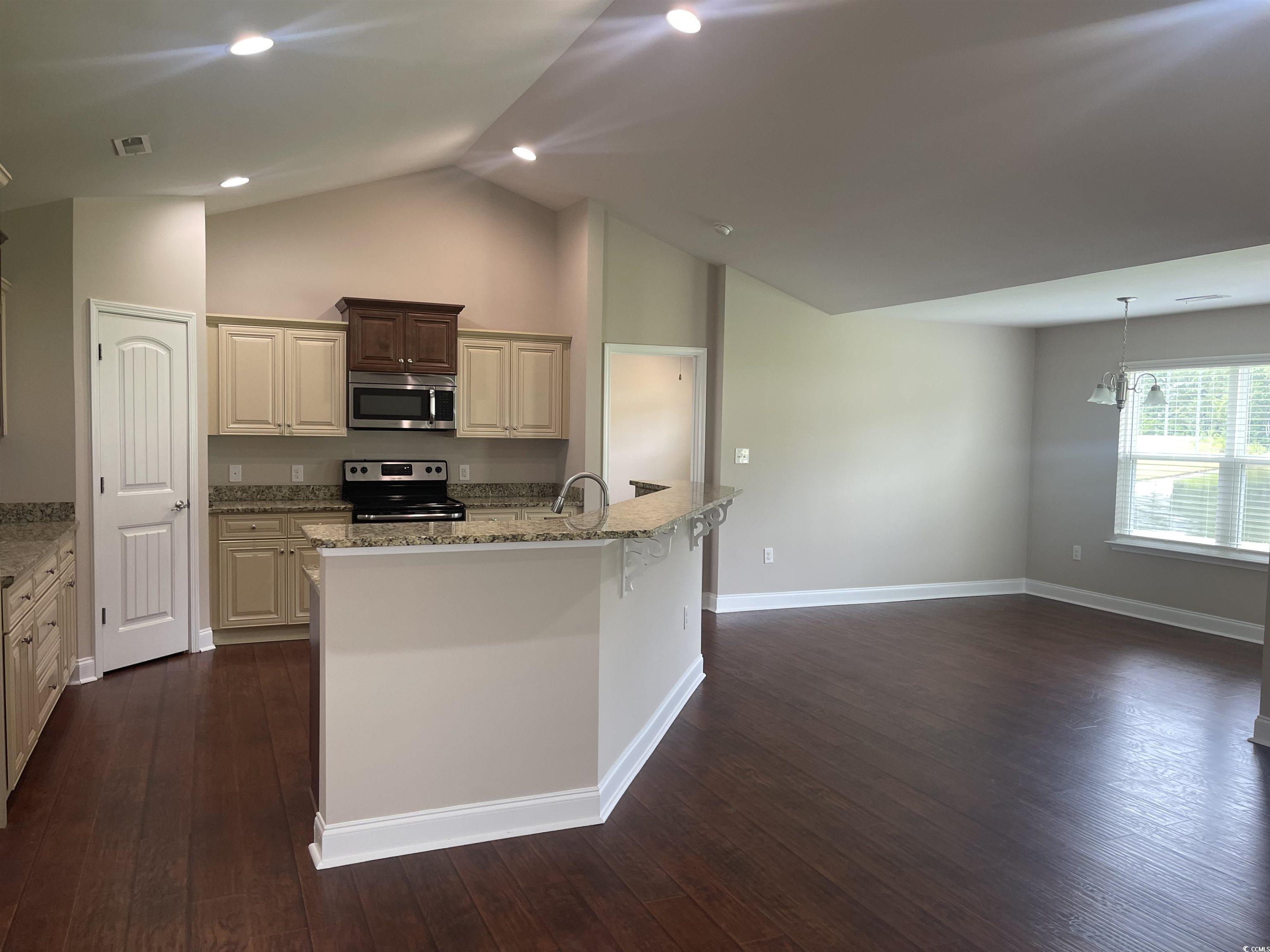 128 Cloey Road Myrtle Beach, SC 29579 - Photo 4 of 22 Kitchen featuring light stone counters, a breakfast bar, appliances with stainless steel finishes, cream cabinets, and vaulted ceiling