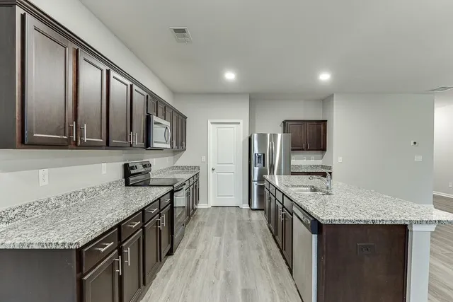 a kitchen with stainless steel appliances granite countertop a stove a sink dishwasher a refrigerator and a microwave oven with wooden floor