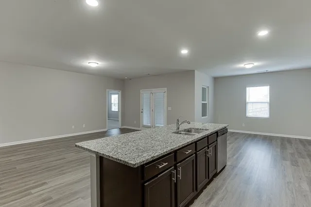 an empty room with wooden floor and kitchen view