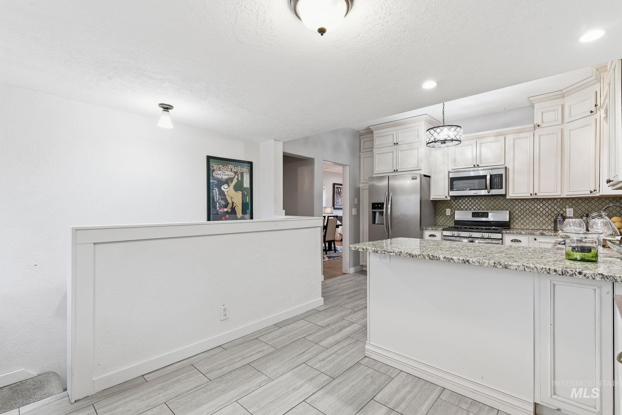 2103 West Bannock Street Boise, ID 83702 - Photo 11 of 49 Kitchen with light stone counters, appliances with stainless steel finishes, tasteful backsplash, a textured ceiling, and a peninsula