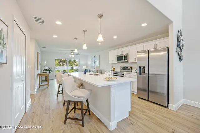 a kitchen with stainless steel appliances kitchen island granite countertop a refrigerator a stove top oven a sink dishwasher and white cabinets with wooden floor