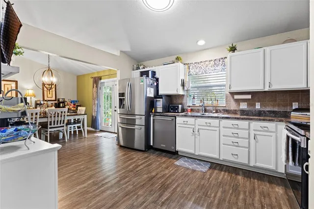 a kitchen with stainless steel appliances a refrigerator a stove a sink dishwasher and a dining table with wooden floor