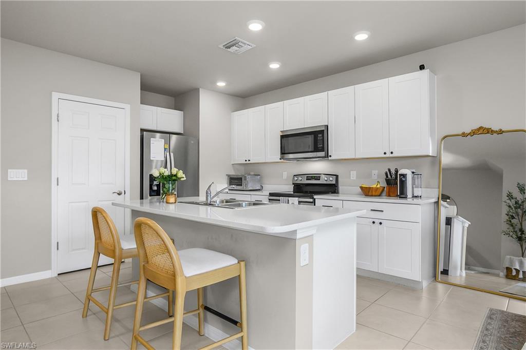 15436 Wildflower Circle Naples, FL 34119 - Photo 14 of 42 Kitchen featuring light countertops, stainless steel appliances, white cabinets, a kitchen breakfast bar, and an island with sink