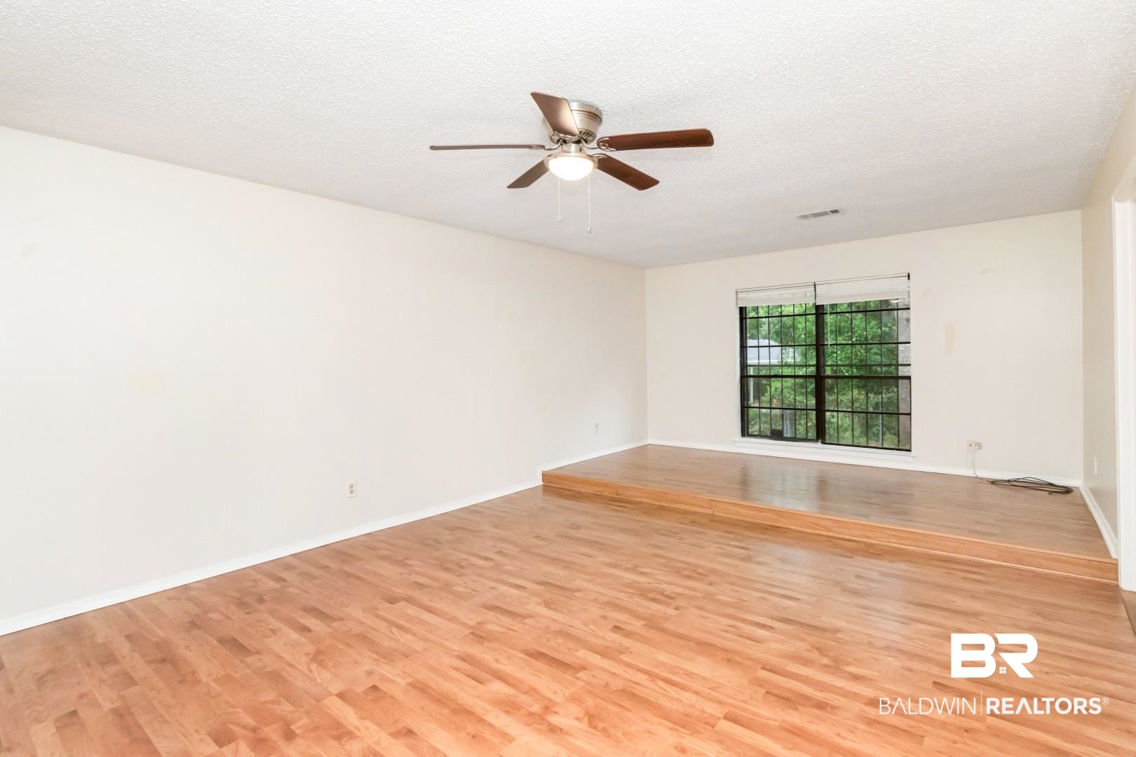 5812 Fern Valley Road Mobile, AL 36609 - Photo 17 of 32 Spacious room featuring wood-finish flooring, a raised platform, a ceiling fan, and a large window with exterior greenery